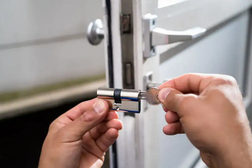 A person’s hands are replacing or installing a door lock cylinder, holding the cylinder in one hand and turning a key with the other, showcasing professional locksmith services NYC with the door slightly open in the background.